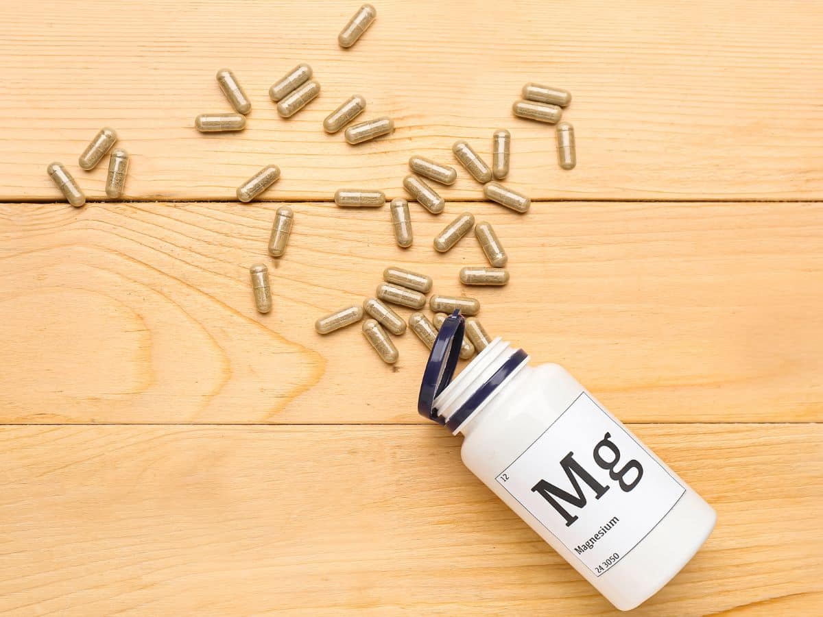A bottle of magnesium and scattered pills on a wooden table.
