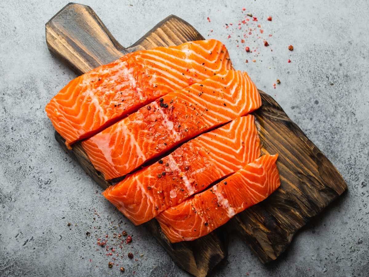 Four pieces of fresh, raw salmon on a cutting board.