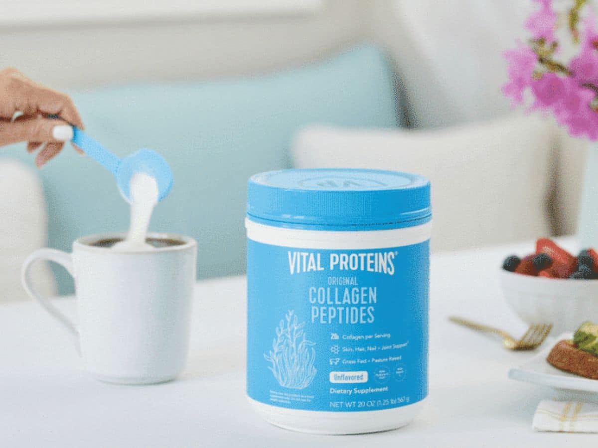 A blue container of Vital Proteins Collagen Peptides with someone pouring the powder into a cup in the background.