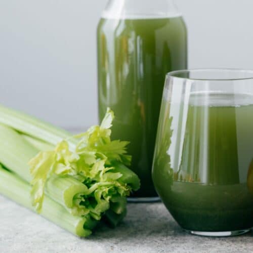 two glass cups of celery juice next to raw celery stalks on light grey counter