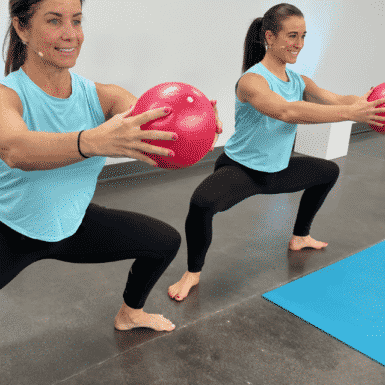 Shelley Hawkins and Sam Cameranesi holding a red pilates ball in a plie squat hold.