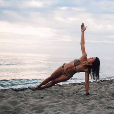 woman doing side plank scoop yoga for core strength on beach
