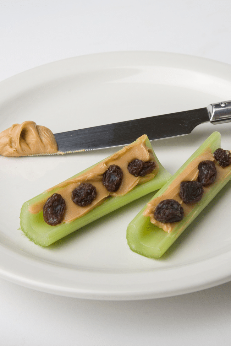 Celery with peanut butter and raisins with a knife on a plate