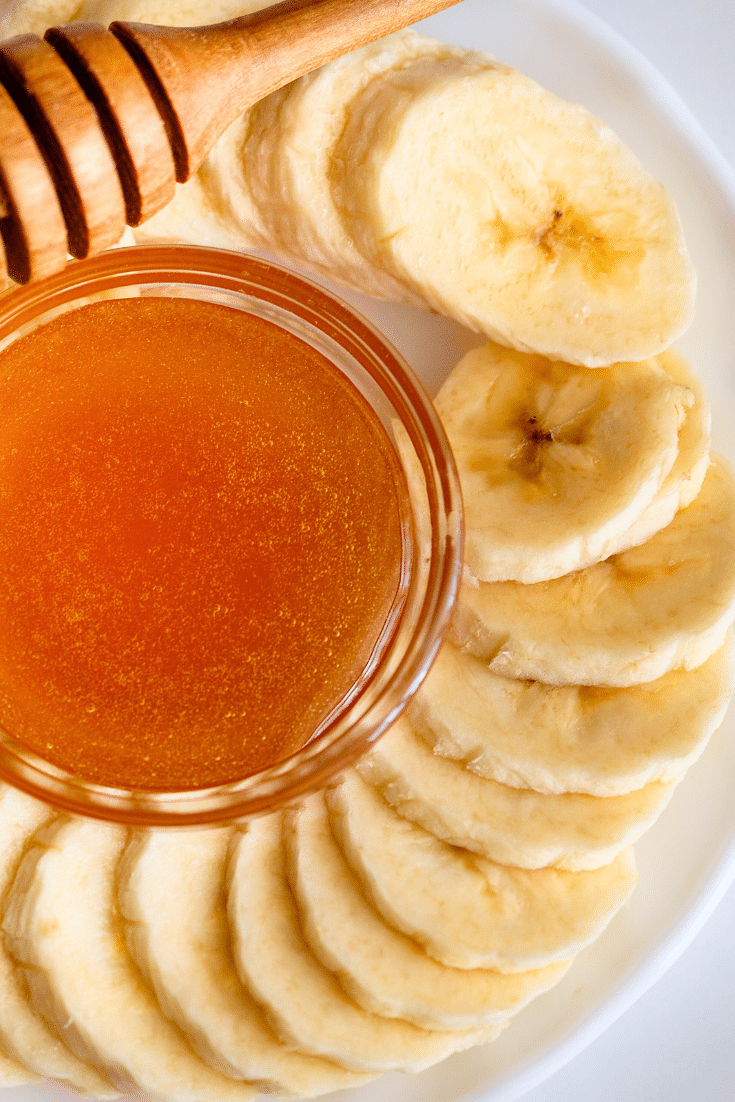Slices of banana on a plate next to a small dish of honey