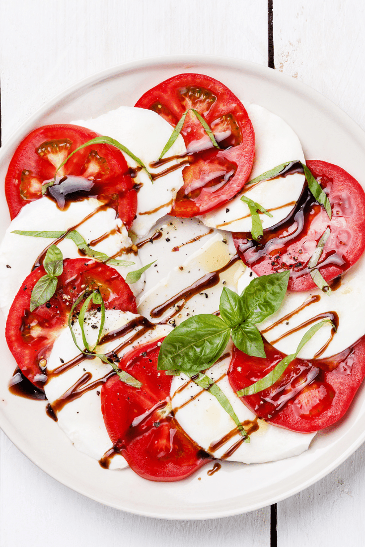 Sliced tomatoes, fresh mozzarella in a circle with basil and olive oil and balsamic