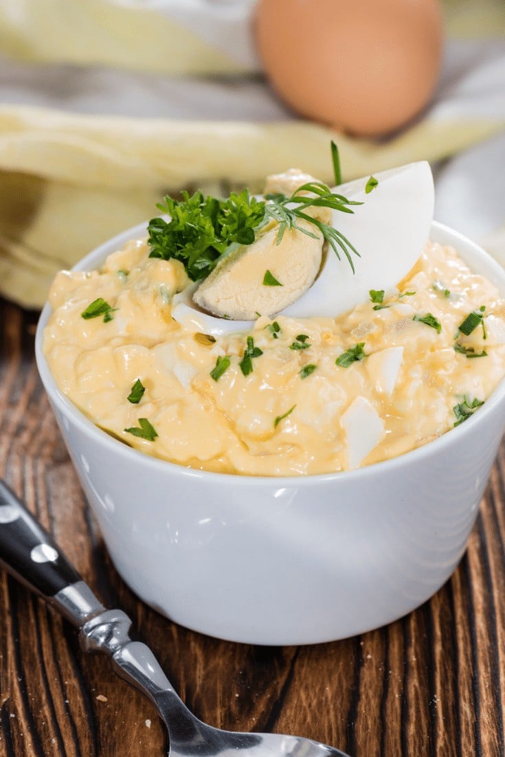 Egg salad in a white bowl with greens on top