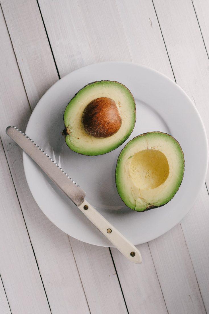 Two halves of an avocado on a white plate with knife
