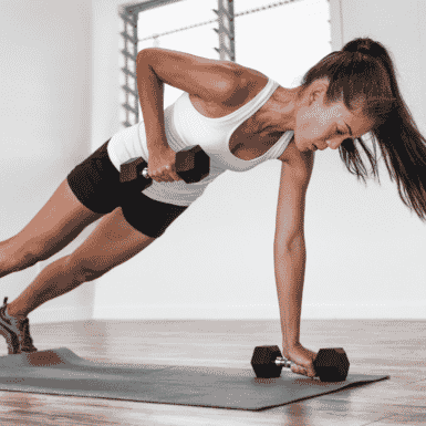 Young woman performing dumbbell renegade row on workout mat
