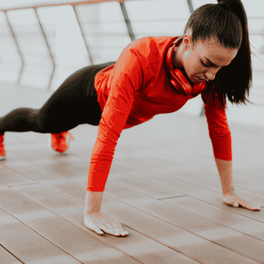 Woman performing a modified burpee in a red long sleeve and black leggings
