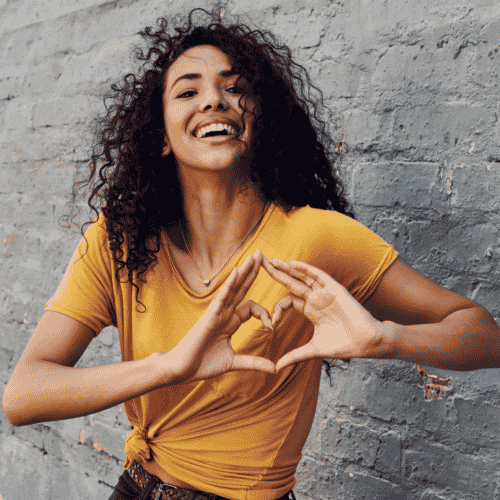 woman in yellow making a heart with her hands