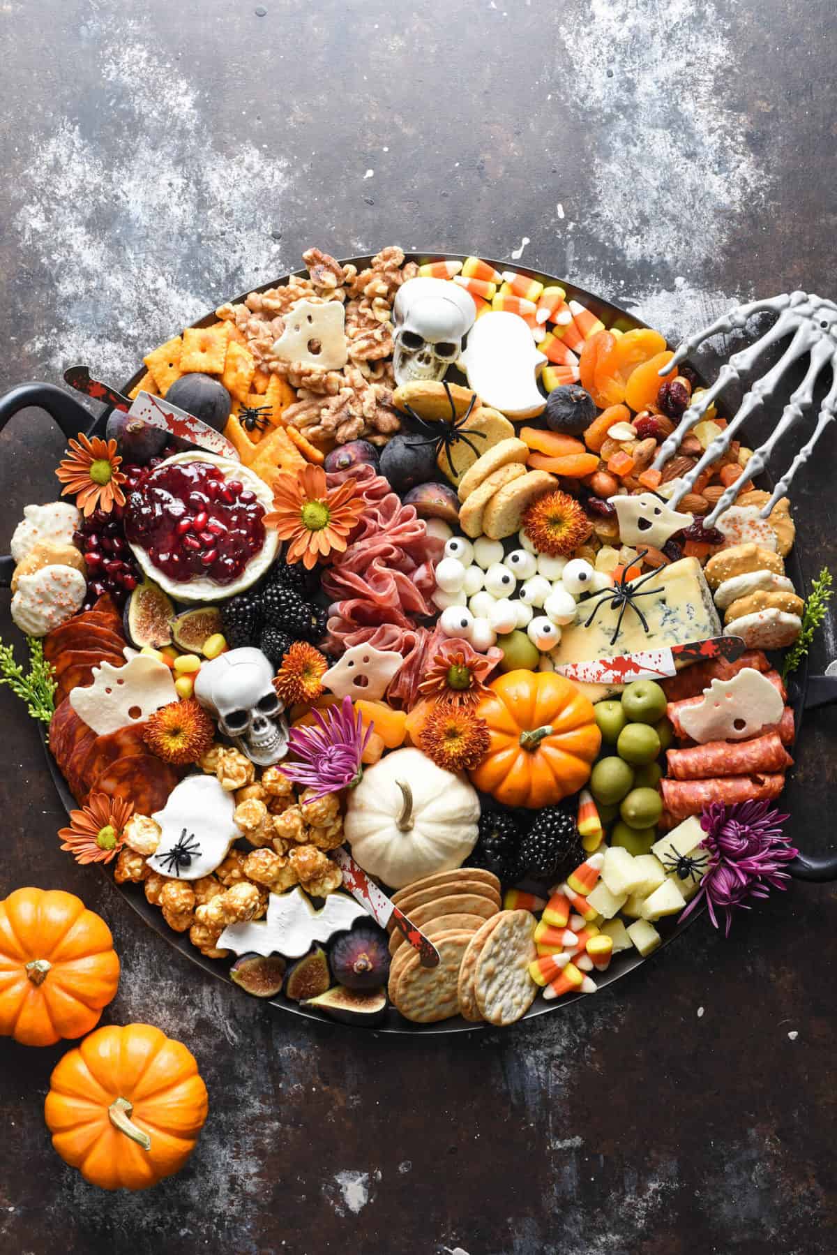 Healthy halloween snack ideas: a large charcuterie board filled with cheeses, meats, pumpkins, candy corns, skulls,, crackers, blackberries, and more