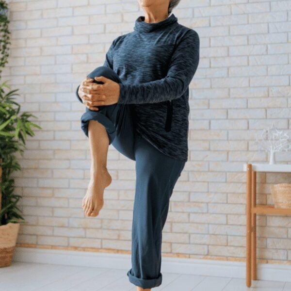 Senior woman performing hip strengthening exercises in living room with dumbbells and laptop