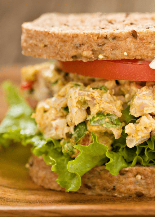 Curry chicken salad closeup in a sandwich on wood platter