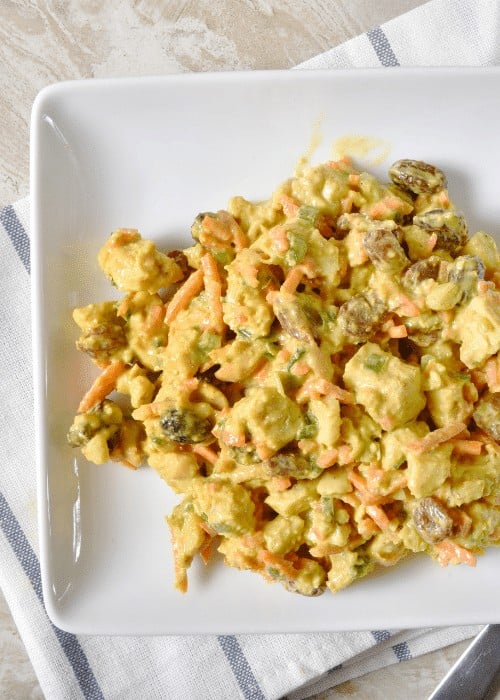 A white plate on a blue and white towel with our copycat recipe for curry chicken salad