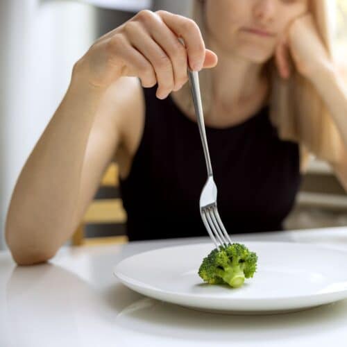 woman looking down at single piece of broccoli on plate looking for expert tips to lose weight without dieting