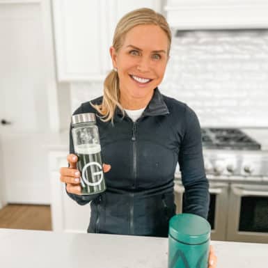 Chris Freytag in her home kitchen holding up a bottle of Athletic Greens
