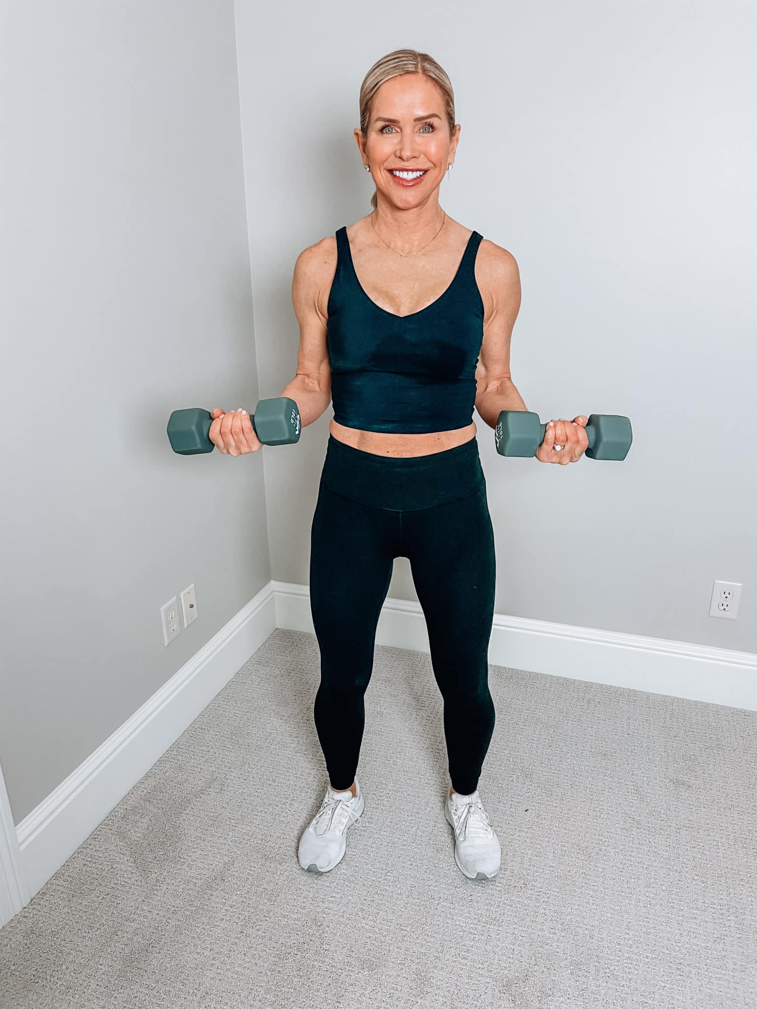 Chris Freytag wearing a black crop top with black leggings holding a pair of grey 10 lb dumbbells.