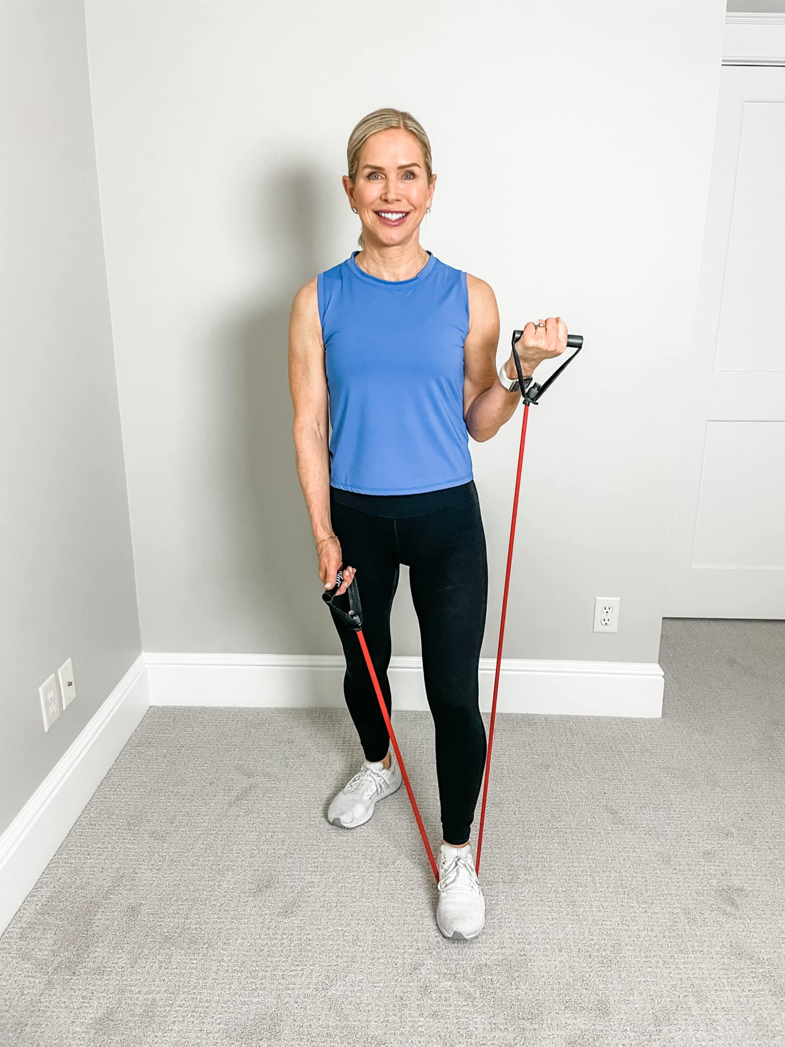 Chris Freytag wearing a blue tank top and black leggings holding a red resistance band for a resistance band workout.