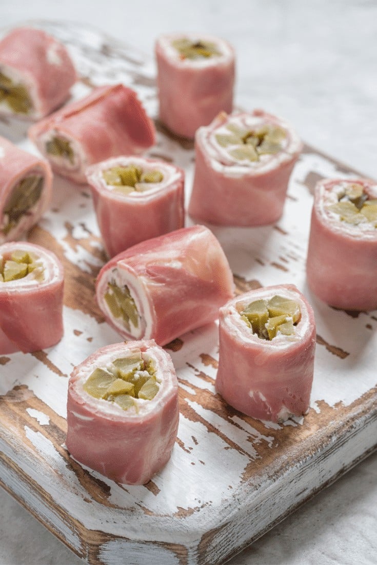 Pickles wrapped in ham with a layer of cream cheese on a serving board