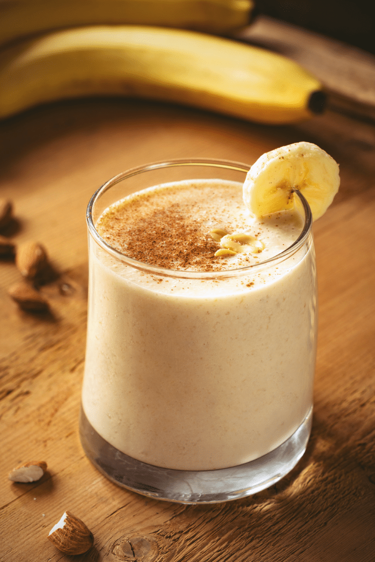 A chocolate banana almond butter smoothie in a glass on a wood serving board