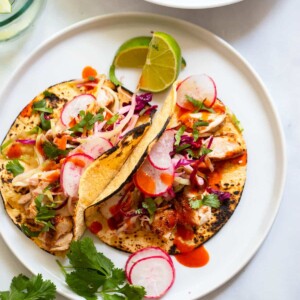 mahi mahi fish tacos topped with slaw and radish on a plate.