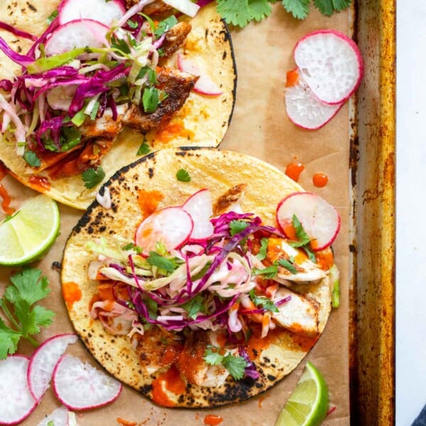 mahi mahi fish tacos garnished with slaw and cilantro on a sheet pan.