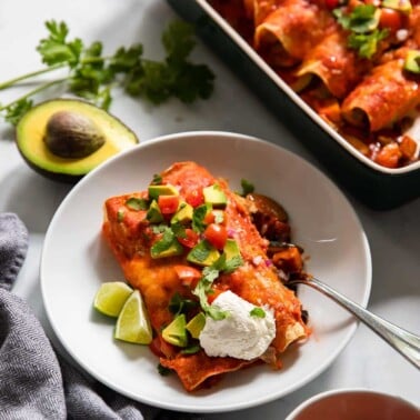 vegetarian black bean enchiladas dished out onto a plate and topped with sour cream and chopped avocado.