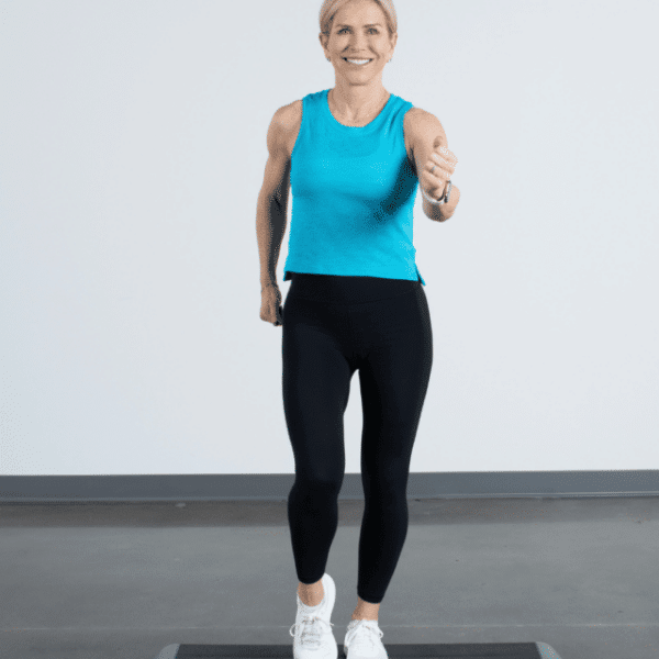 Chris Freytag wearing a blue tank top and black leggings, doing a step move on a step platform.