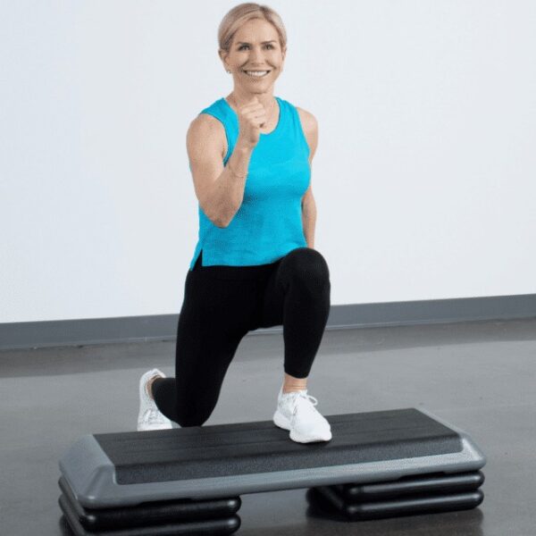 Chris Freytag wearing a blue tank top and black leggings doing a lunge with her front foot on a step platform.