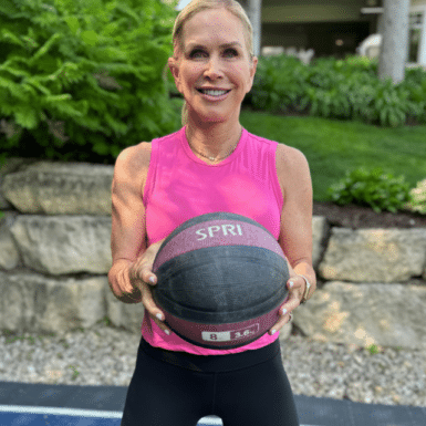 Chris Freytag wearing a pink workout tank, holding an 8 lb SPRI medicine ball for a medicine ball total body workout.