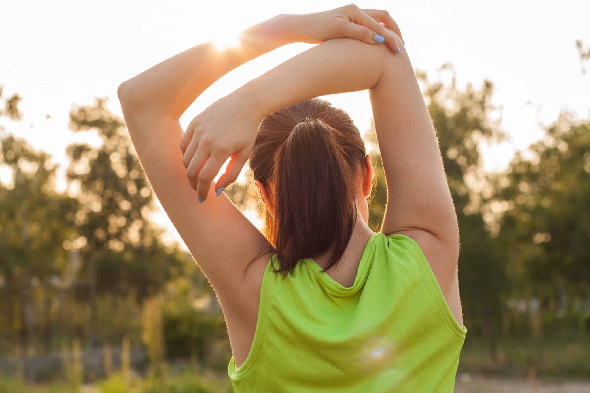 A view of the back of a woman stretching outside.