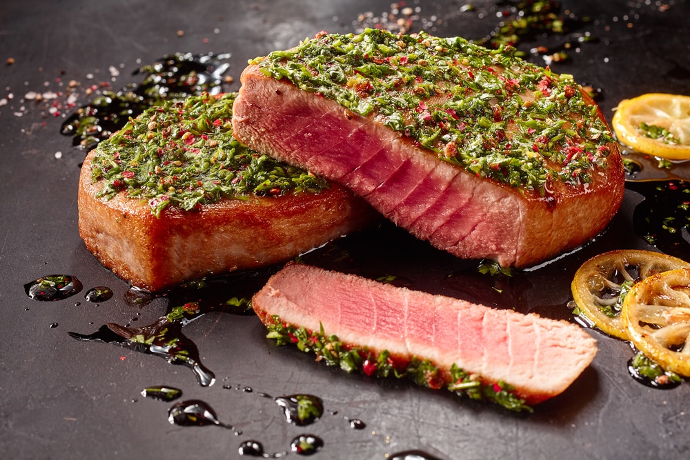 A close-up view of two tuna steaks topped with herbs.