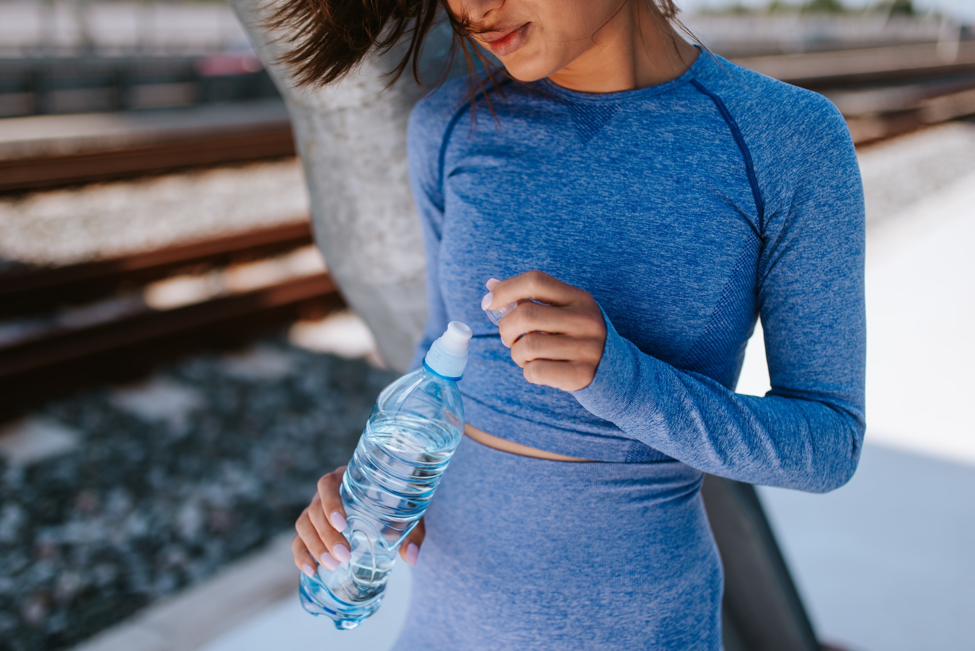 Woman in blue workout clothes resting against a tree holding a bottle of water.