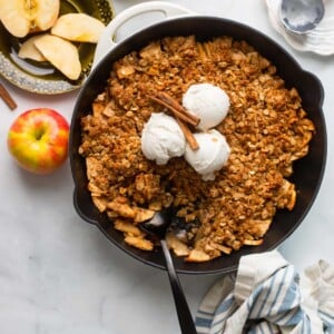 healthy apple crisp in a skillet topped with 3 scoops vanilla ice cream and cinnamon sticks.