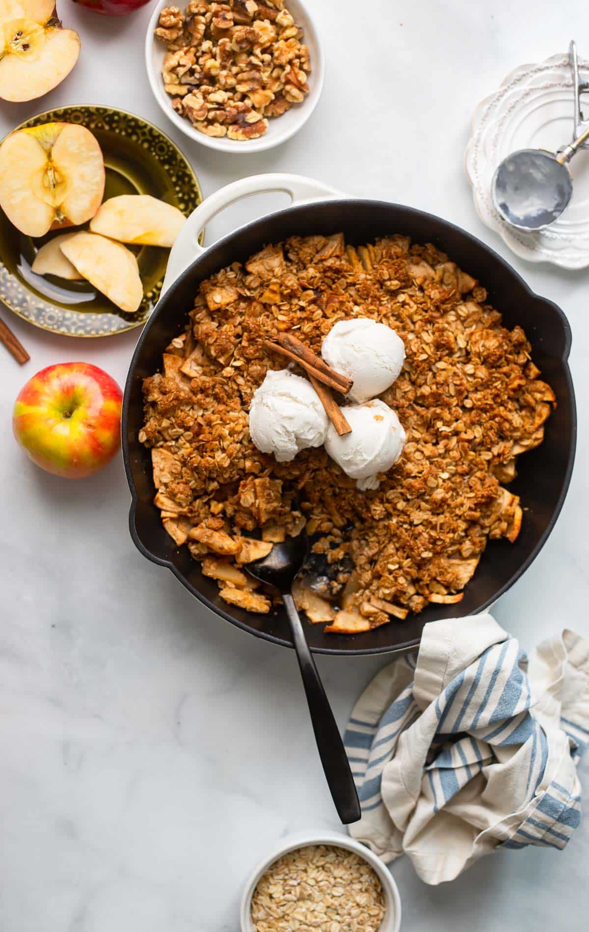 baked healthy apple crisp in skillet topped with 3 scoops of vanilla ice cream.