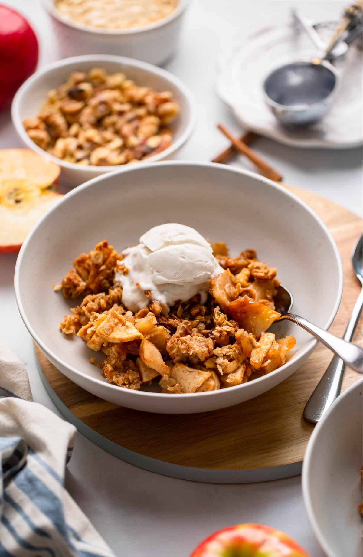 healthy apple crisp dished into a low bowl and topped with a scoop of vanilla ice cream.