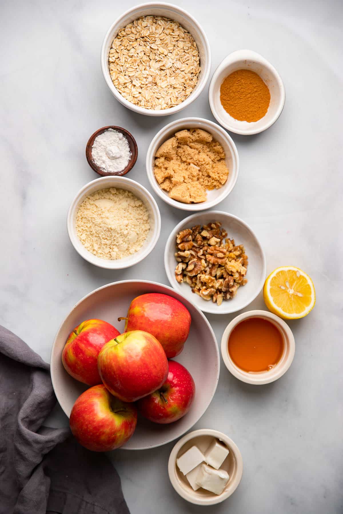 healthy apple crisp ingredients in small bowls on a white background.