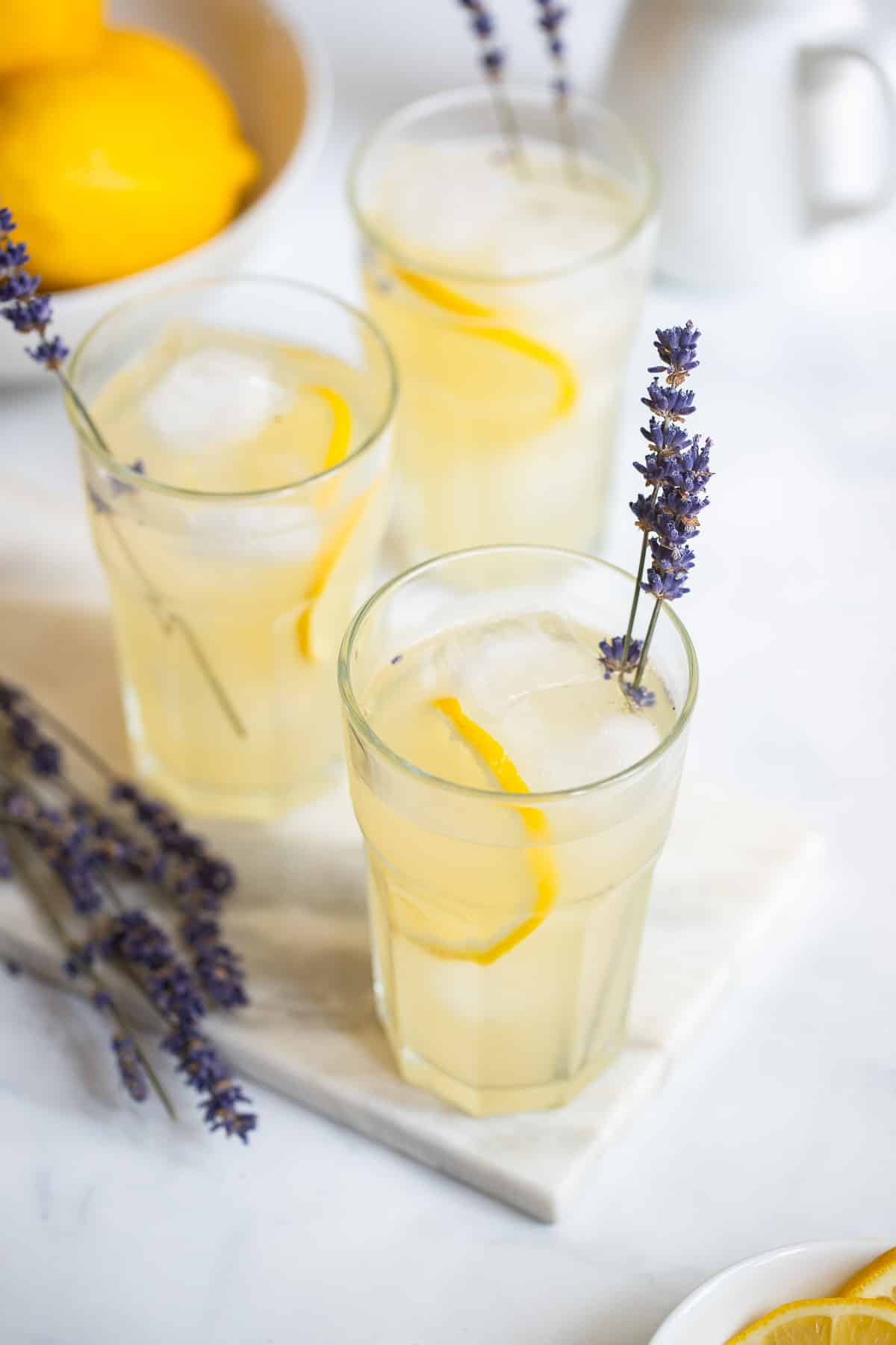 lavender lemonade in tall glass with ice garnished with lemon slice and a sprig of fresh lavender.