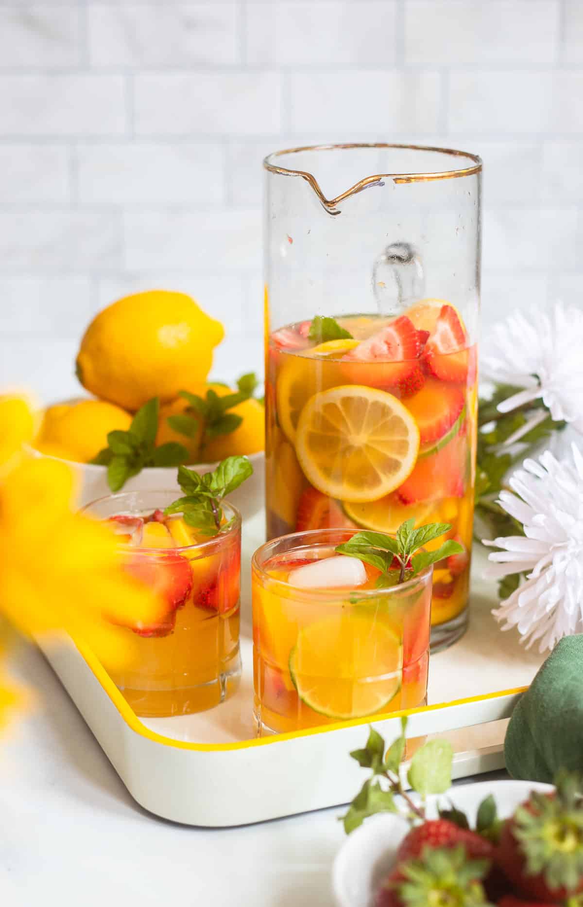 strawberry mango sangria in a tall pitcher on a tray with two glasses of sangria garnished with mint.