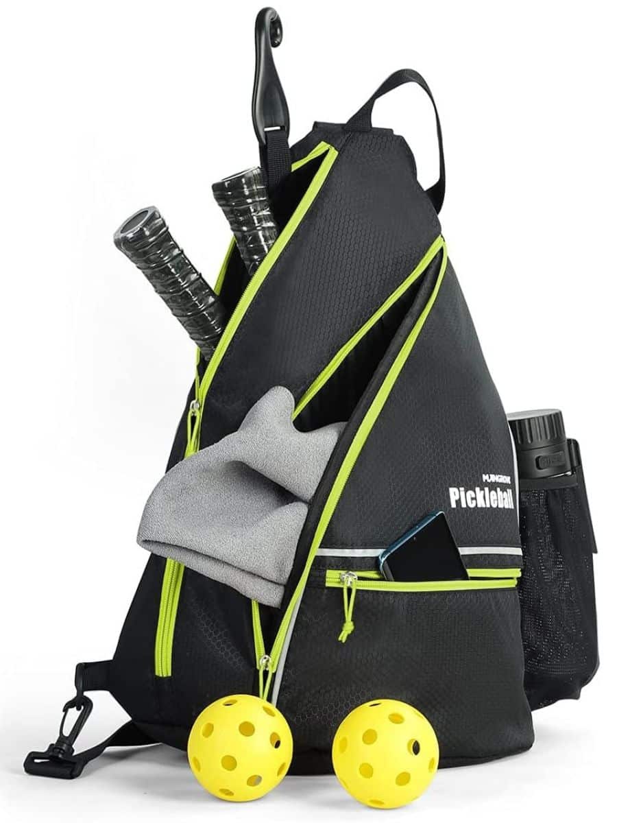 A black and neon Mangrove pickeball bag holding a phone and two pickleball paddles inside, with two yellow pickleballs sitting in front.
