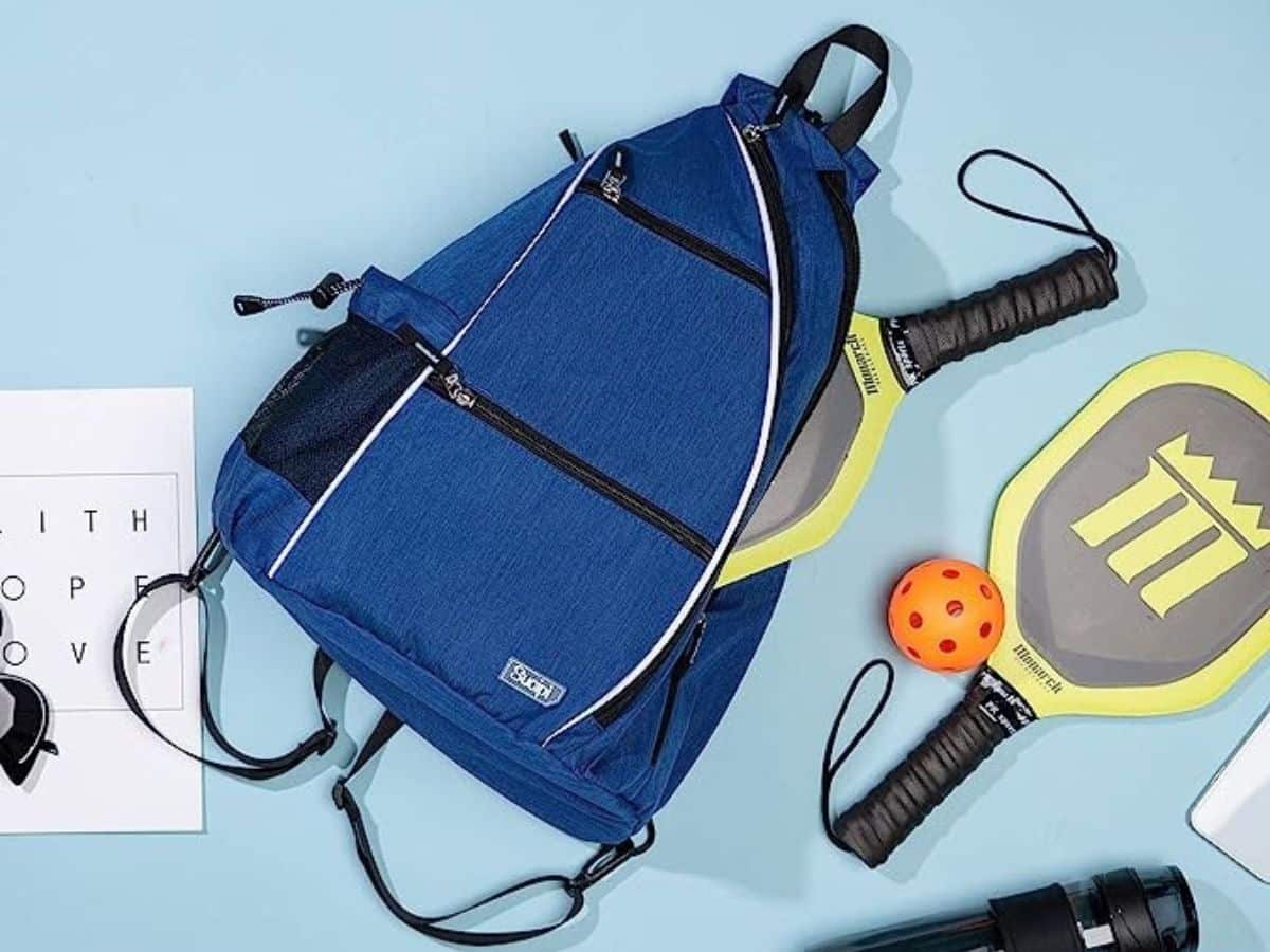 A blue Sucipi pickleball bag on a contrasting blue background next to two pickleball paddles and an orange pickleball.