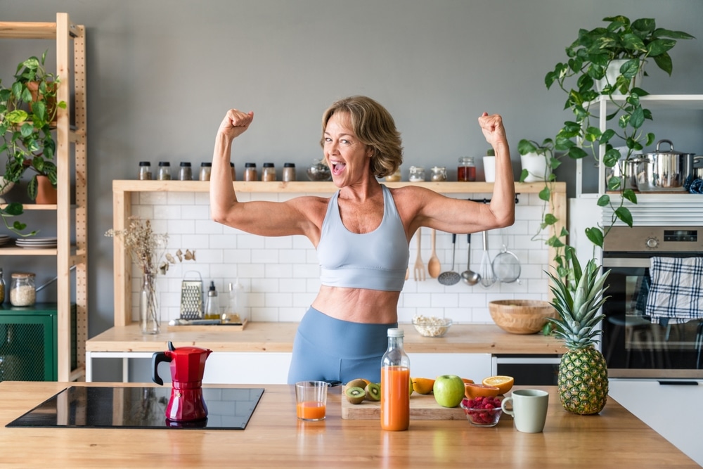 Woman flexing her arm muscles in the kitchen.