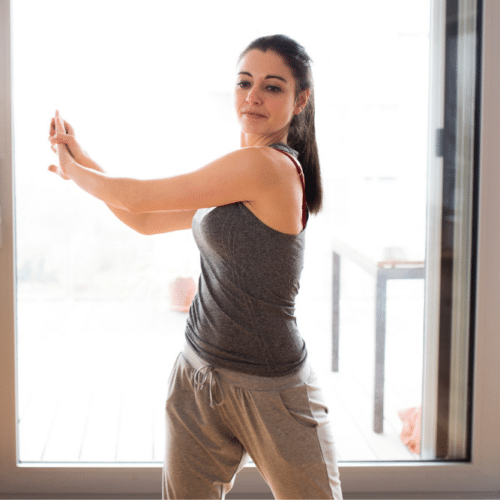 A woman stretching in a tank top and sweatpants.