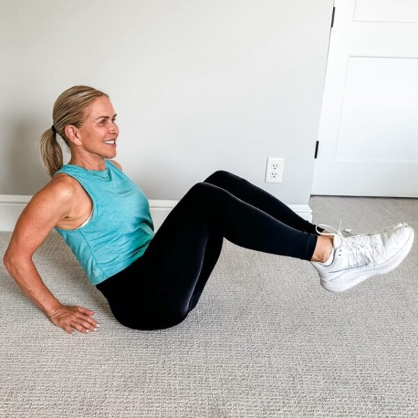 Chris Freytag wearing a blue tank top and black leggings holding an ab tuck position for low ab workout.