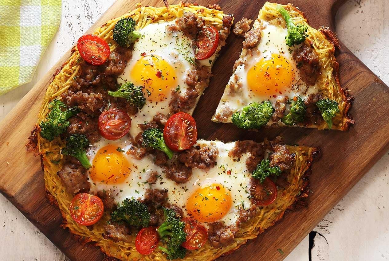 A paleo breakfast pizza, with eggs, sweet potato, tomatoes, broccoli, and sausage.