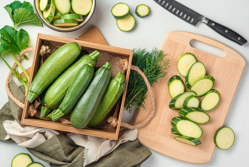 Sliced zucchini on a cutting board next to a basket of whole zucchinis.