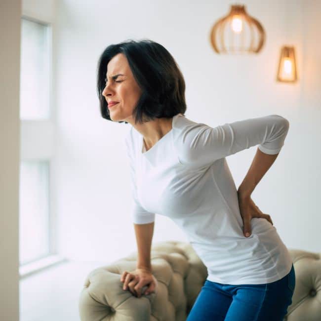 woman standing bent over holding lower back with painful expression on face