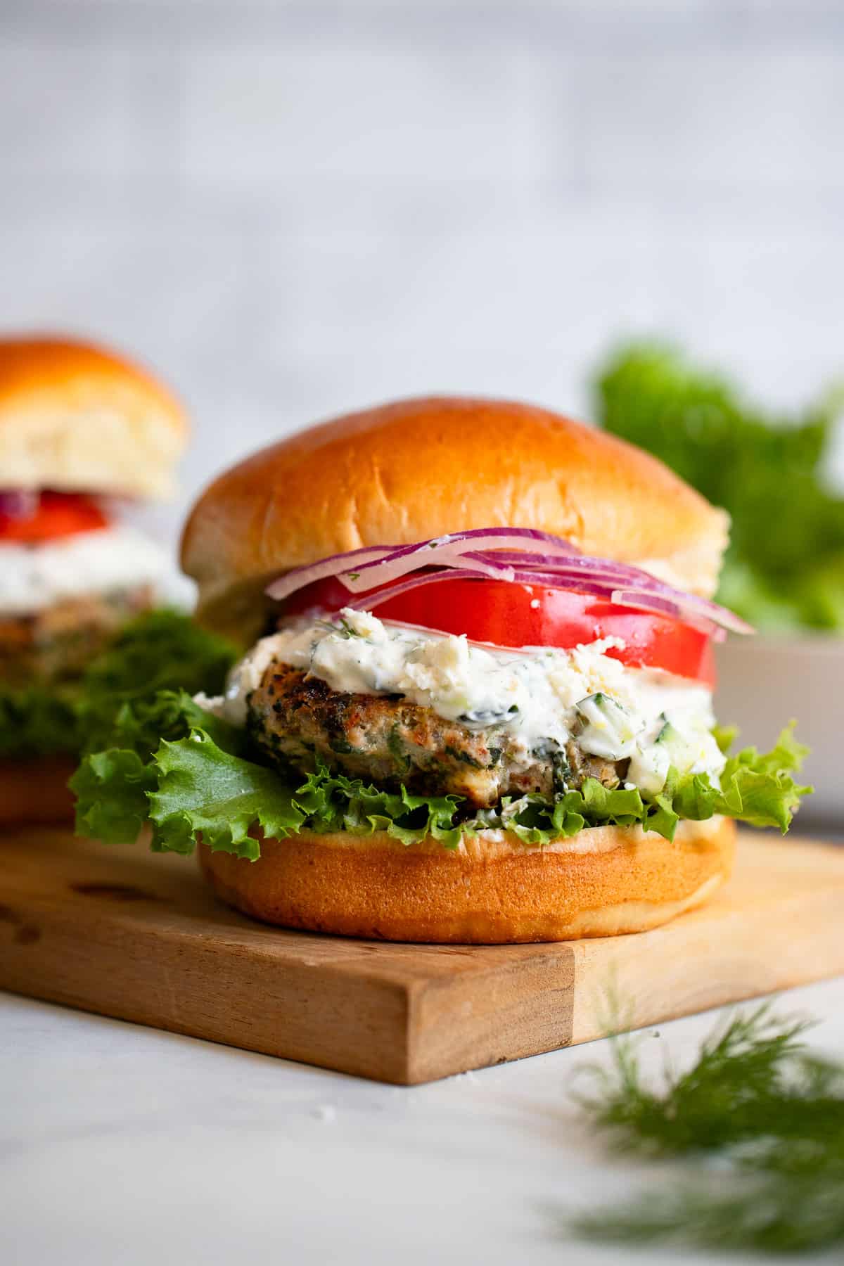 close up show of greek turkey burger with tzatziki with toppings on wooden block