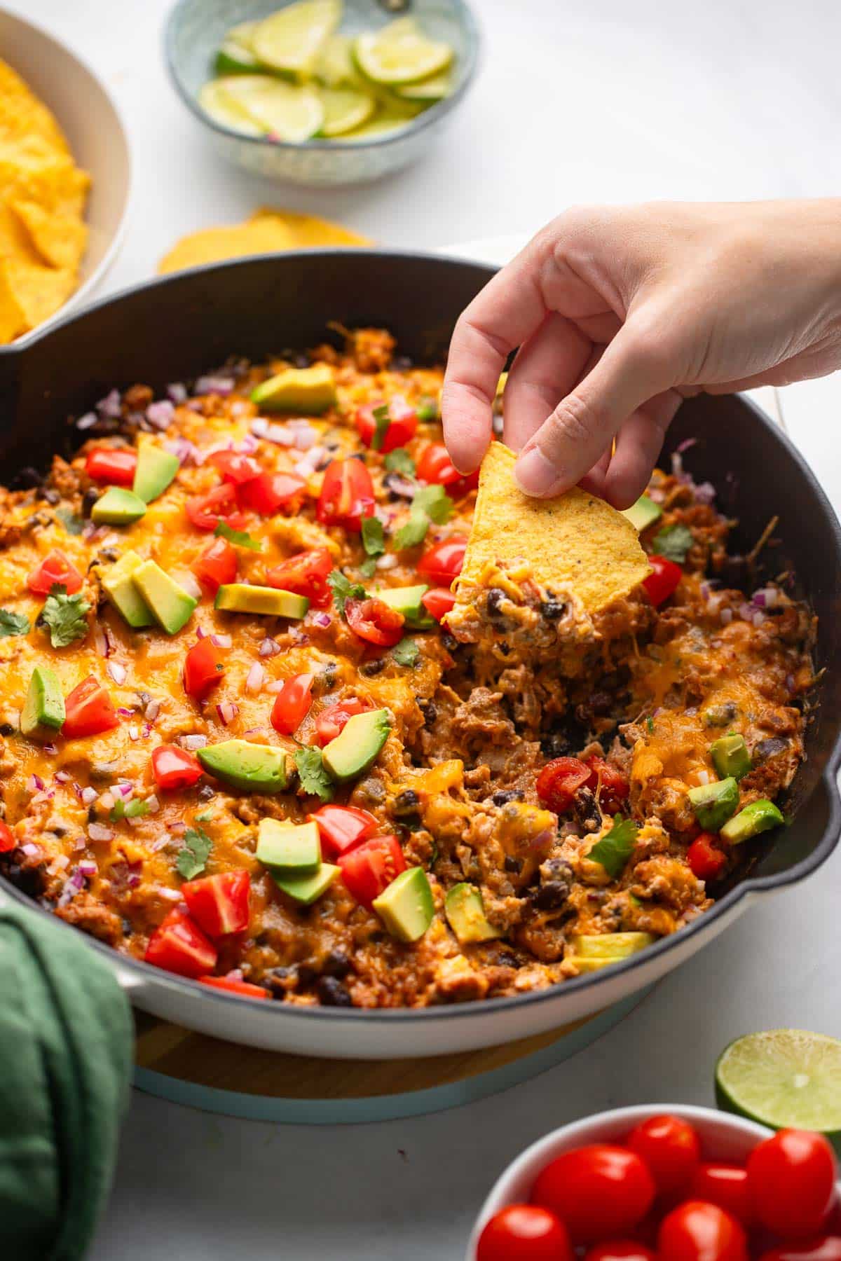 hand dipping chip into healthy chili cheese dip in pan on white counter