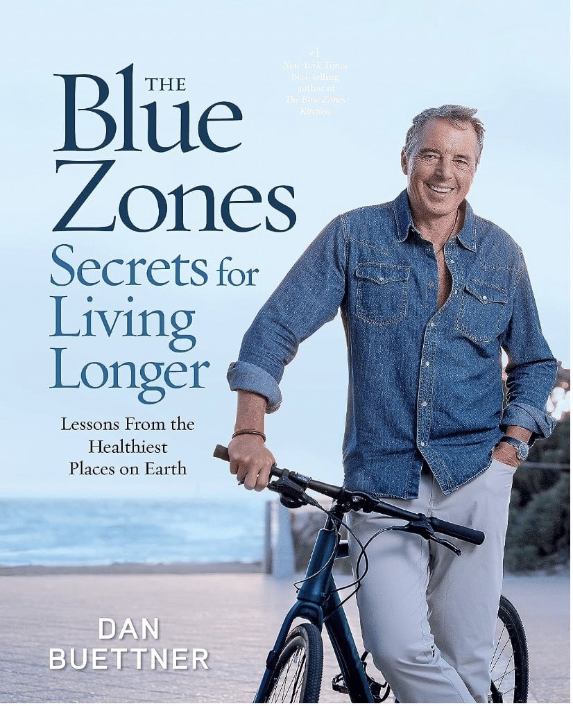 Photo of the book "The Blue Zones Secrets for Living Longer" by Dan Buettner with blue background and man holding onto a black bike. 